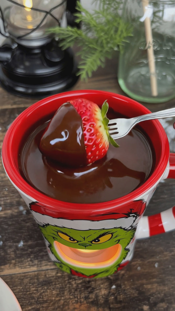 Dipping a strawberry into melted chocolate in the Grinch chocolate melter mug